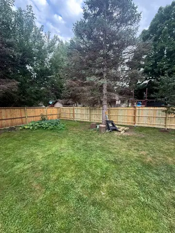 Spacious fenced backyard with lush green grass and trees