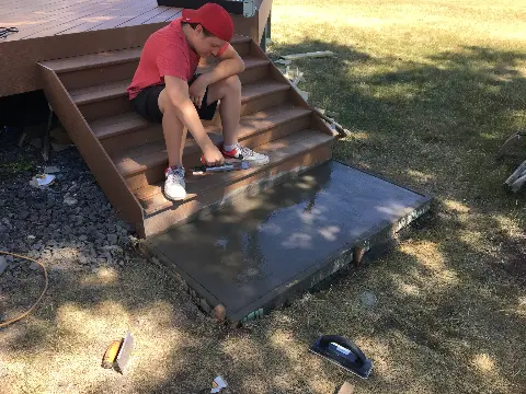 Teenager smoothing concrete slab on outdoor steps in backyard